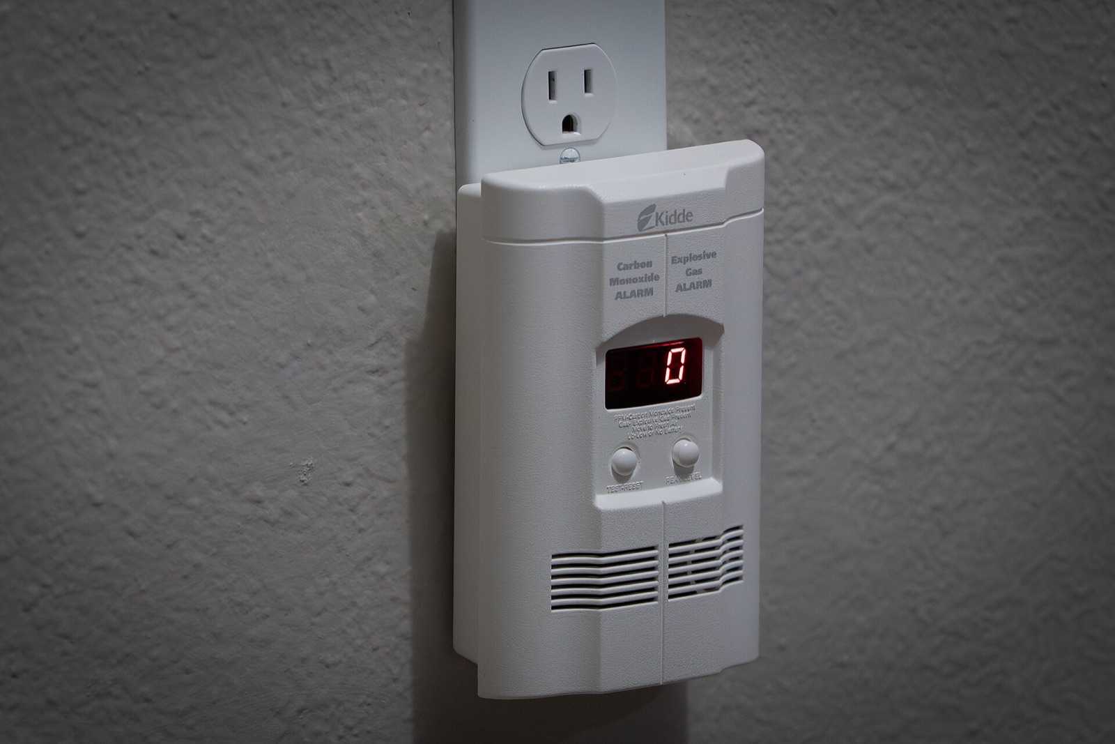 Plug-in carbon monoxide and explosive gas alarm with a digital display reading 0, mounted below a wall outlet