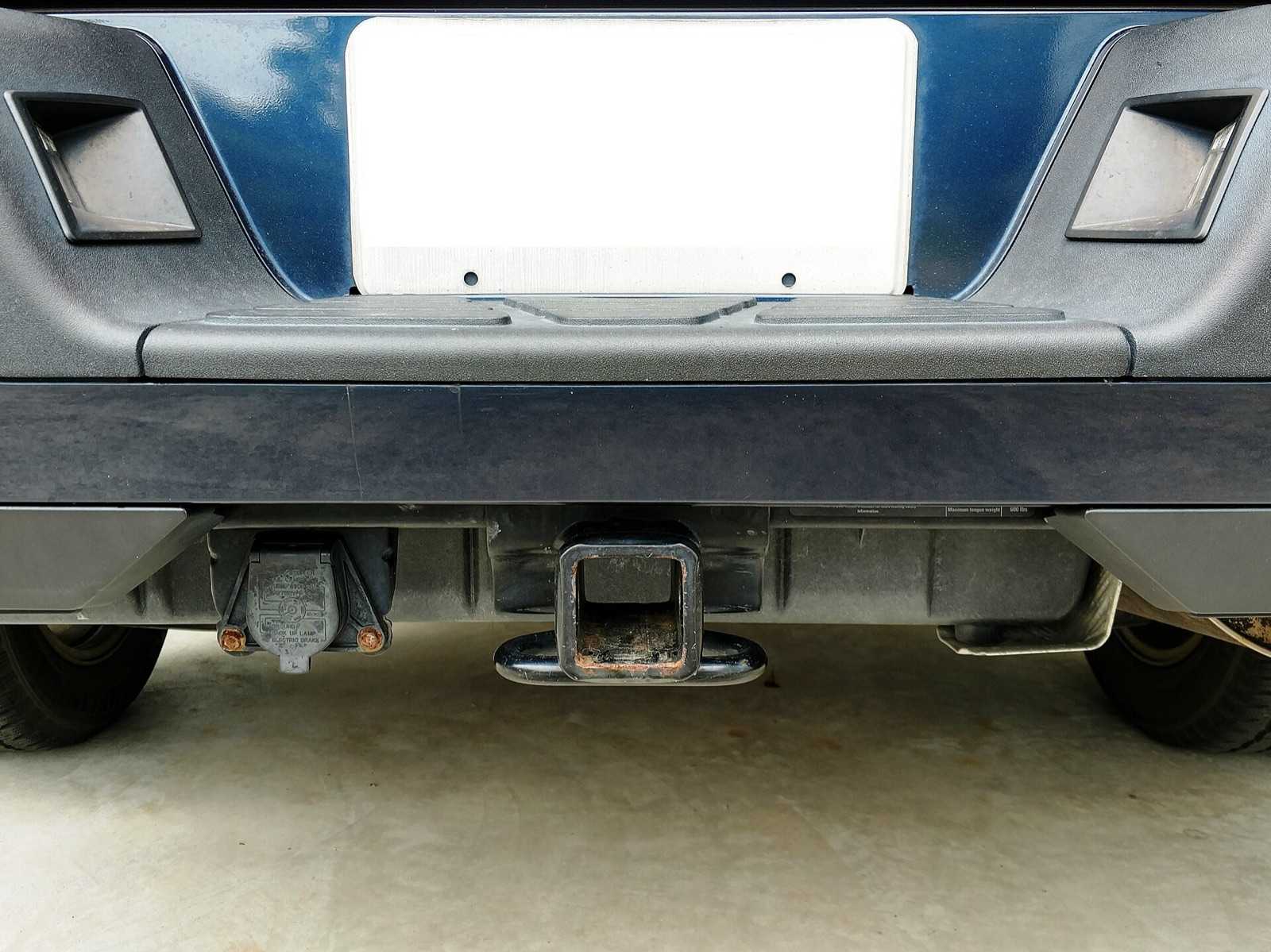 Rear of a pickup showing a 7-way RV blade trailer socket with its flip lid closed, mounted beside a 2-inch receiver hitch