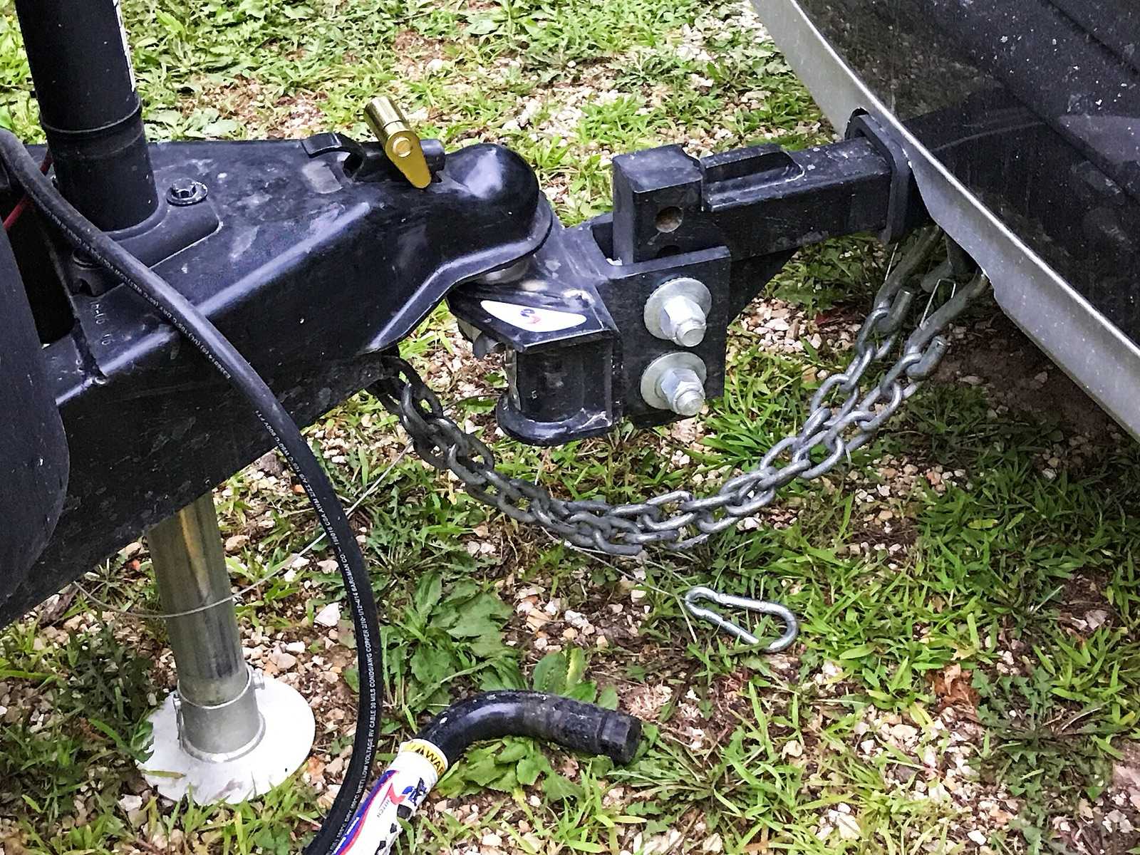 Travel trailer coupler seated on an adjustable ball mount, safety chains hooked to the receiver, and the tongue jack foot resting on a pad in the grass