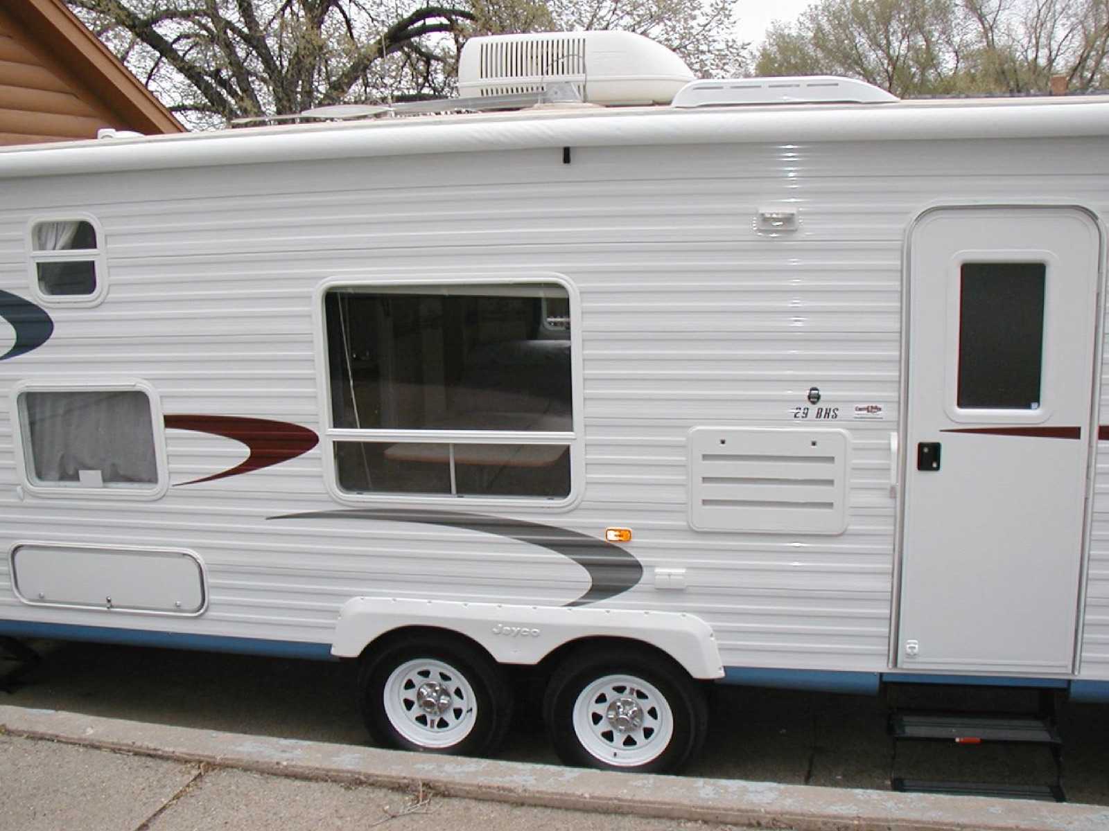 Side view of a white travel trailer with a rooftop air conditioner shroud visible on the roof above the entry door