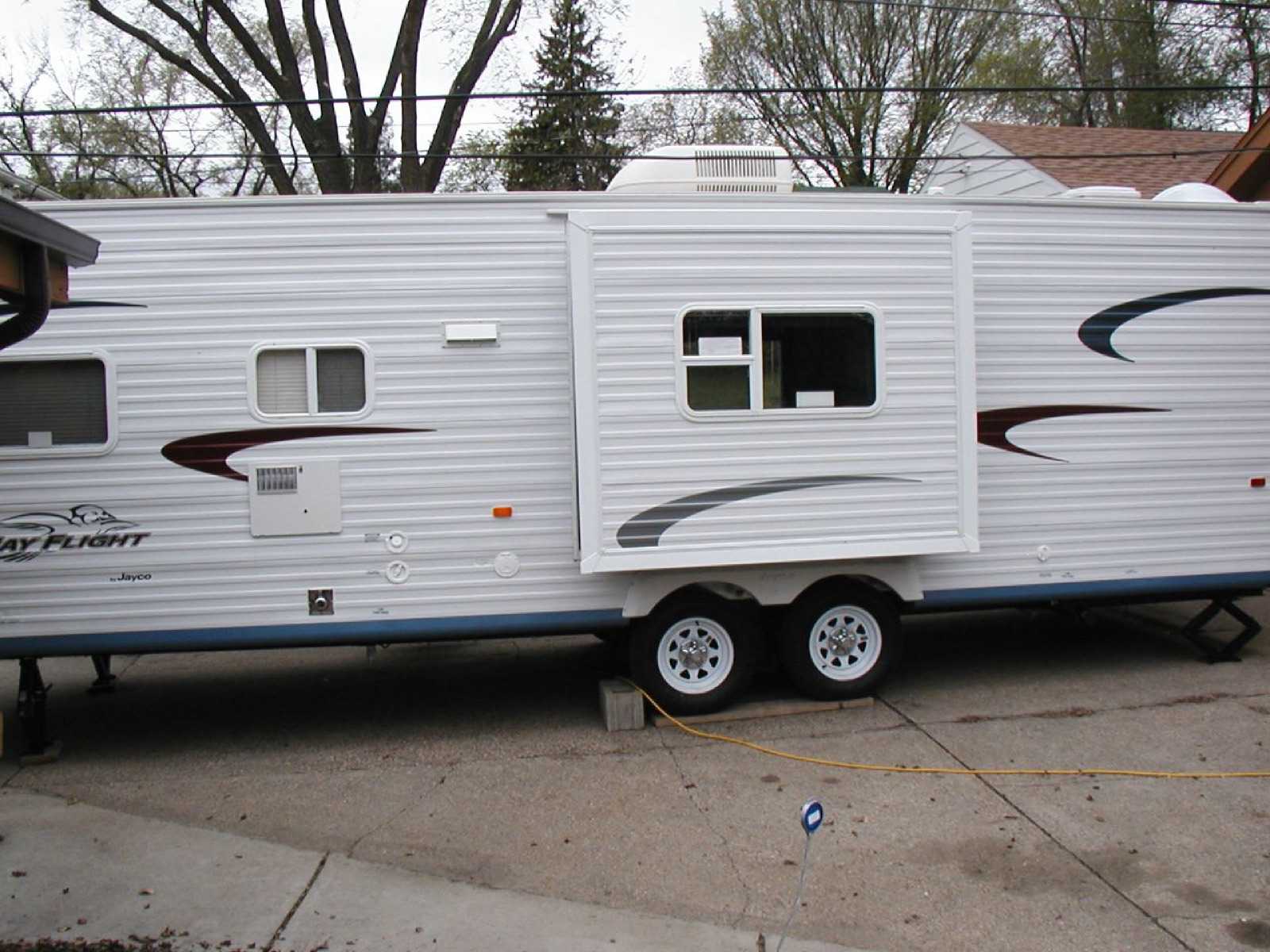 Travel trailer parked on a driveway with its curb-side slide-out room extended, showing the slide's exterior walls and the trim around the opening