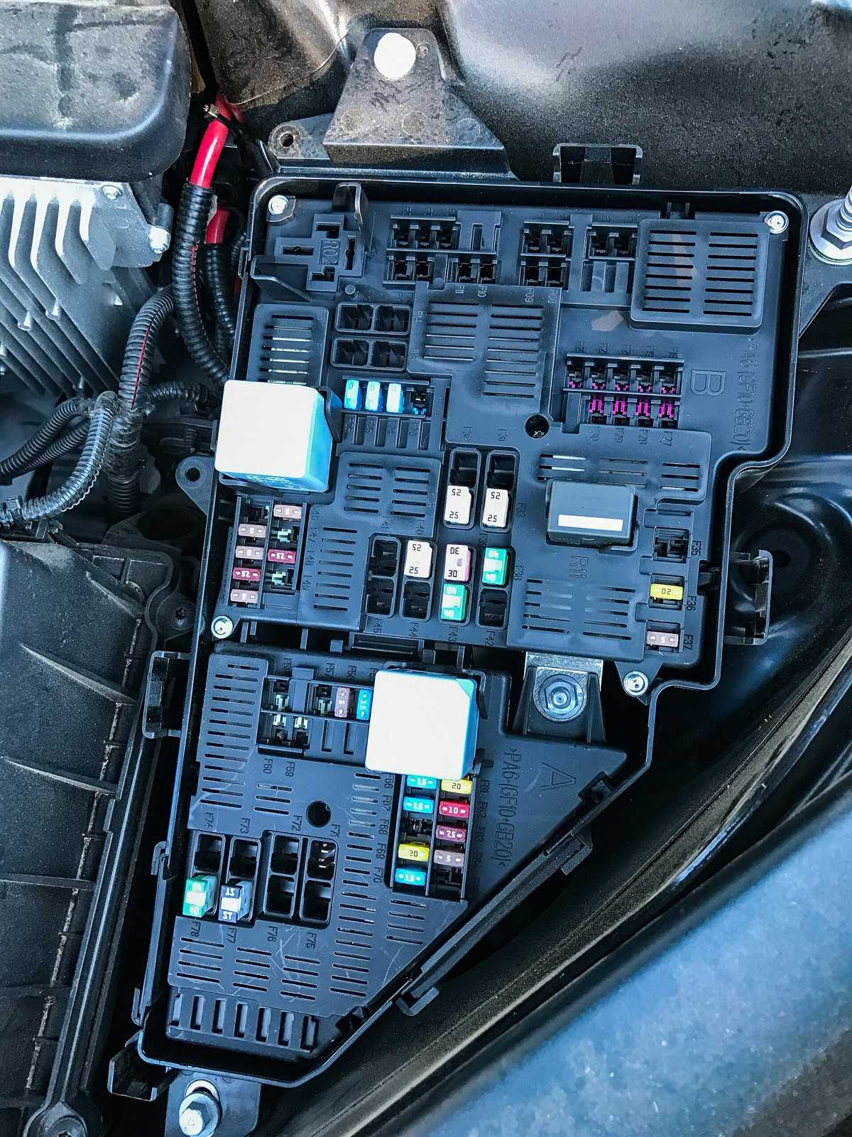 Underhood fuse and relay box on a vehicle with the lid removed, showing rows of blade fuses, mini fuses, and relays